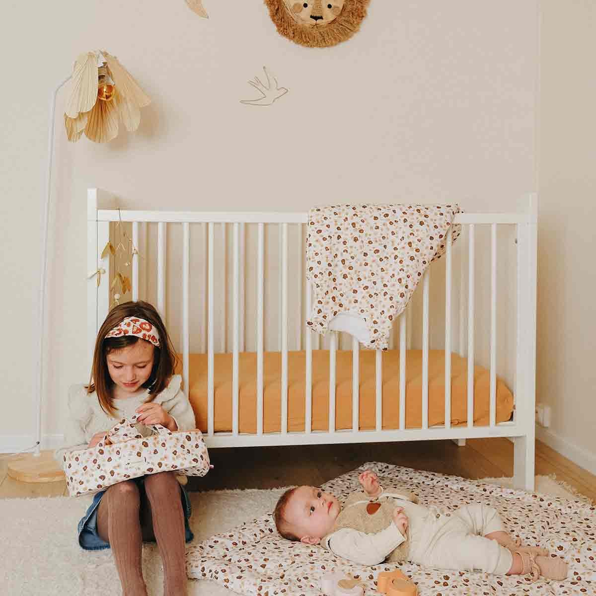 Chambre d'enfant avec linge de lit imprimé léopard, une fillette et un bébé sur un tapis