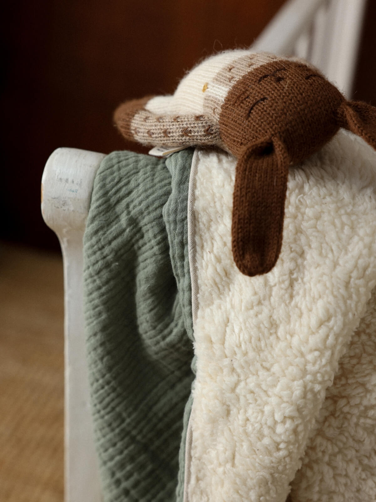 Couverture bébé vert sauge en gaze de coton et polaire sherpa, posée sur un lit avec un doudou