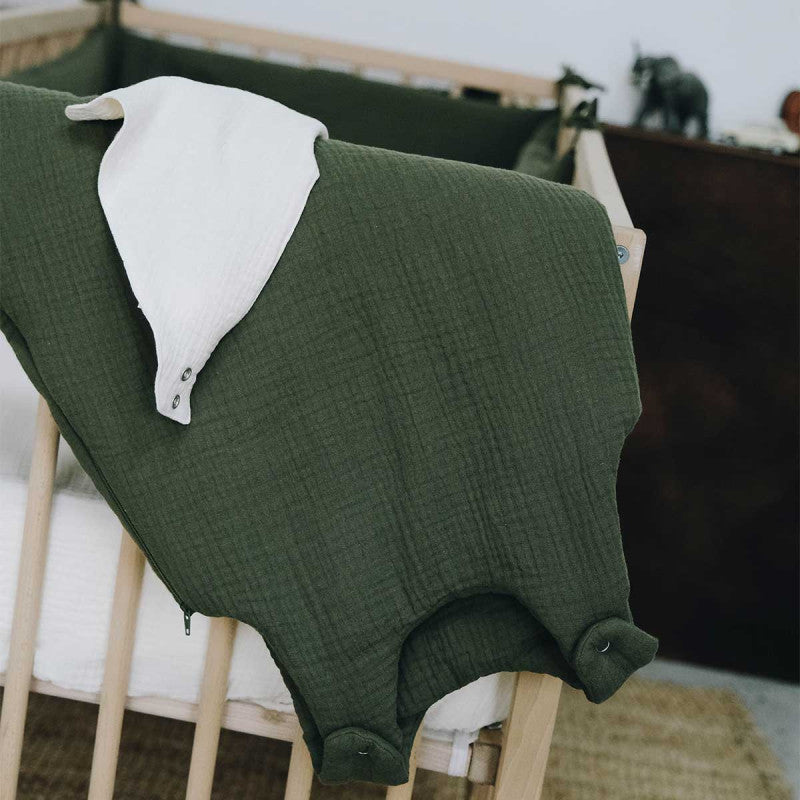 Gigoteuse en gaze de coton vert fougère et son bavoir blanc, posés sur un lit bébé