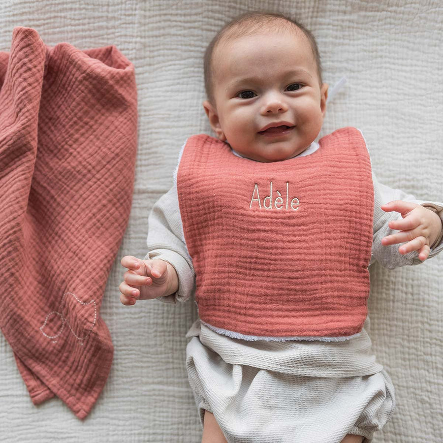 Bébé souriant portant un bavoir marsala brodé au prénom Adèle