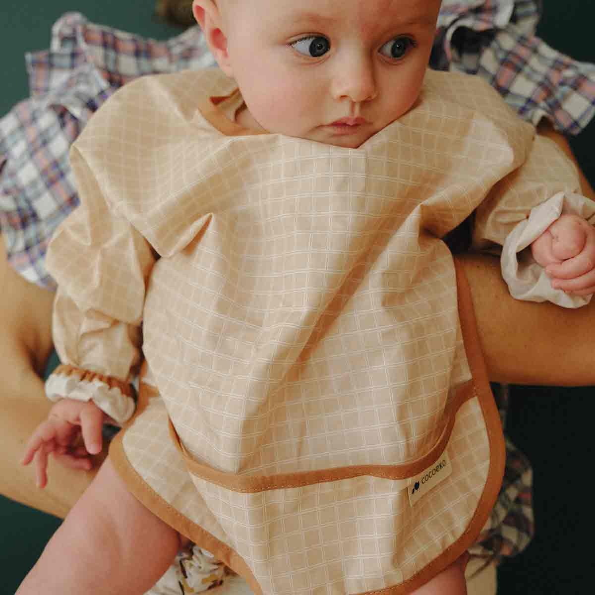 Baby lying down with long-sleeved bib in nude check pattern