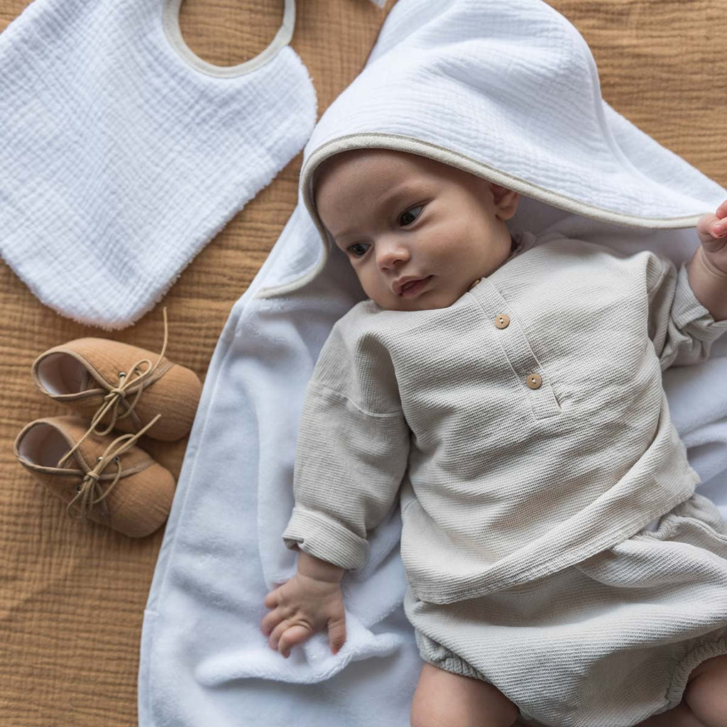 Bébé allongé sur une cape de bain blanche, à côté d'un bavoir et de chaussons