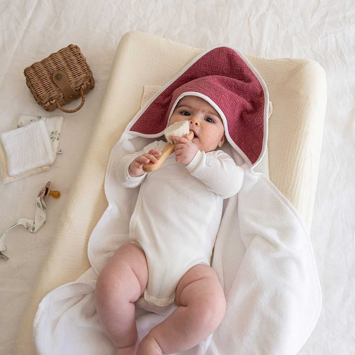 Bébé allongé sur une cape de bain brodée framboise