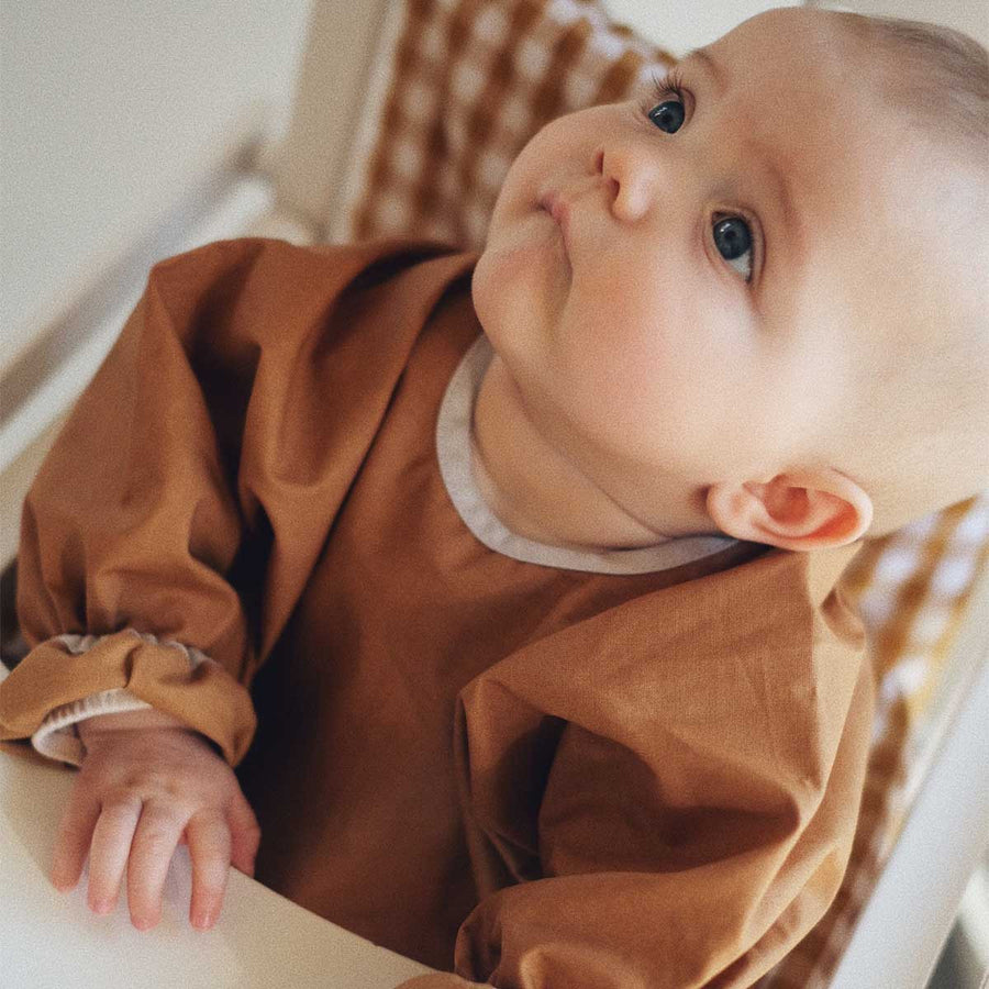 Bébé en bavoir à manches camel dans sa chaise haute