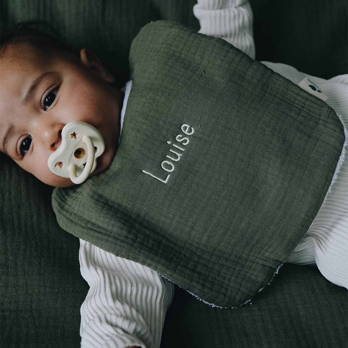 Bébé avec un bavoir vert fougère brodé au prénom Louise
