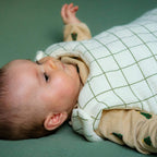 A close-up of a baby wearing a green-checked cotton gauze sleeping bag.