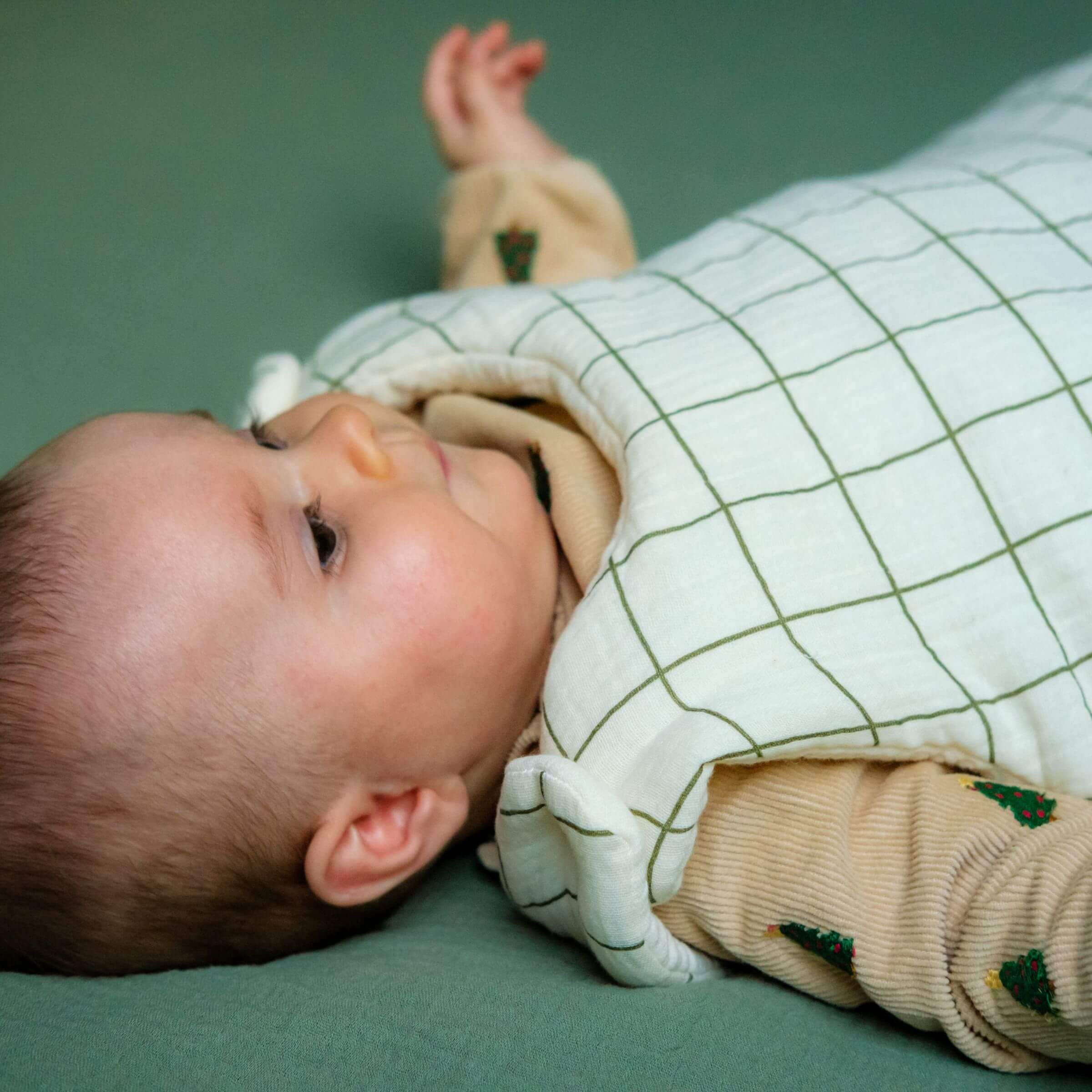 A close-up of a baby wearing a green-checked cotton gauze sleeping bag.