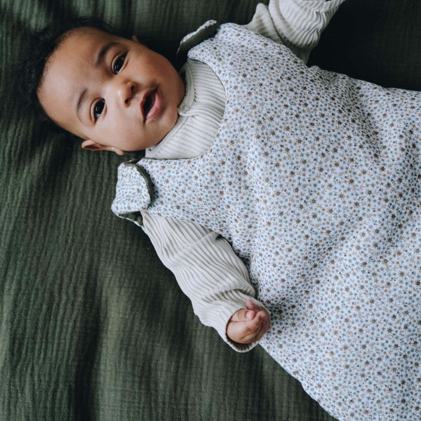 Bébé avec gigoteuse gaze de coton fleurie pour l'hiver dans son lit