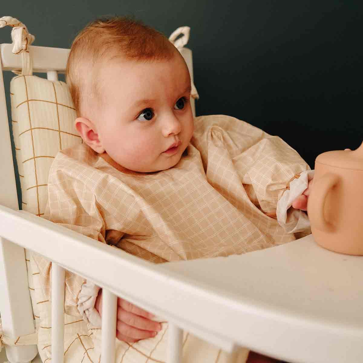 Baby in long-sleeved bib with nude check pattern