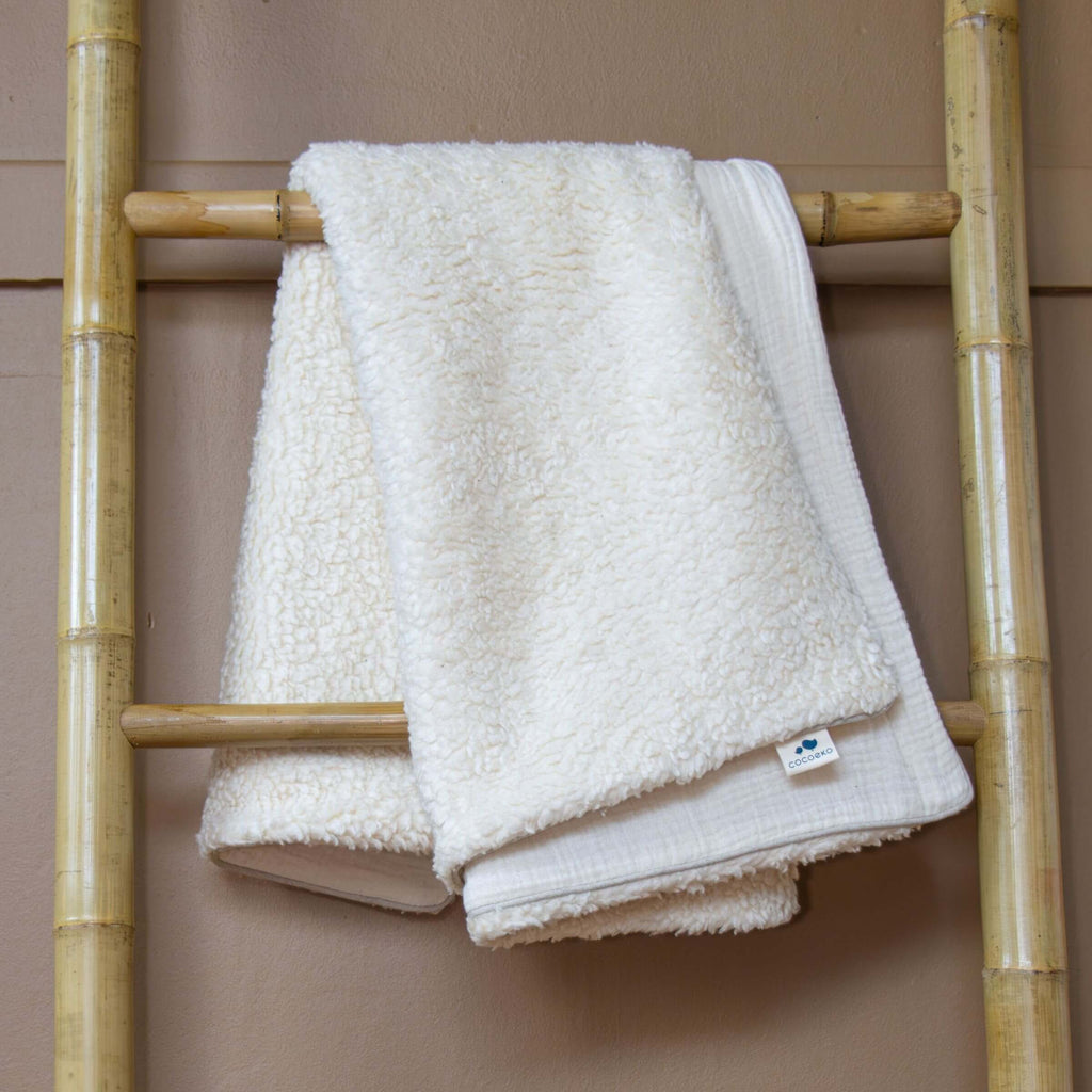Ecru baby blanket hanging from a bamboo ladder, with a sherpa fleece side