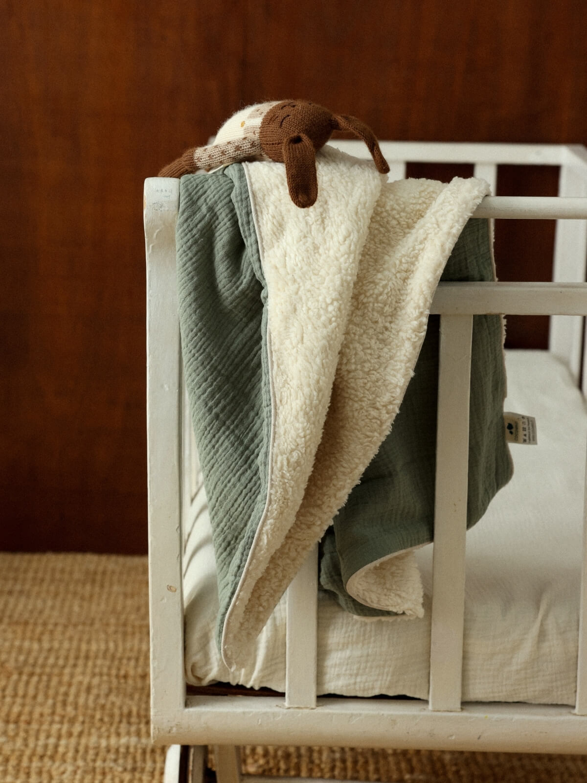 Couverture bébé personnalisable vert sauge, en gaze de coton et polaire, posée sur un lit à barreaux