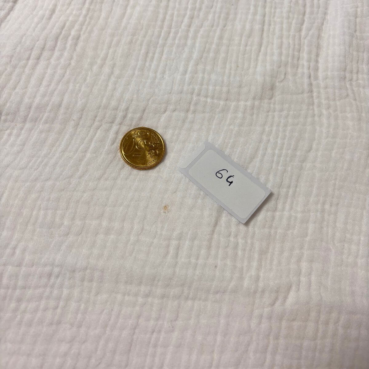 Petite tache sur la gaze de coton blanche d'un drap housse imparfait, pièce de 20 centimes pour l'échelle