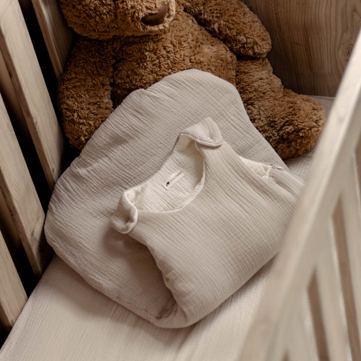 Gigoteuse d'hiver de couleur beige et écru dans lit bébé avec un doudou