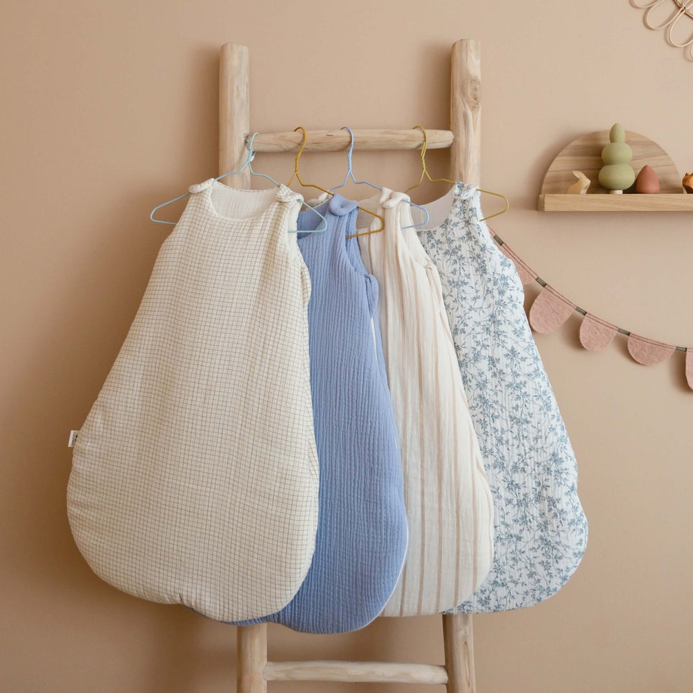 Quatre gigoteuses en gaze de coton, à carreaux, bleue, rayée et à fleurs, suspendues à une échelle en bois dans une chambre de bébé