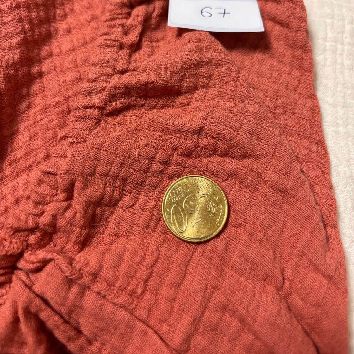 Défaut sur la gaze de coton marsala d'une housse de matelas à langer imparfaite, pièce de 10 centimes pour l'échelle