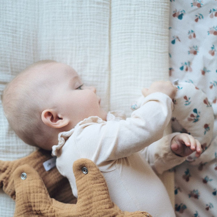 Bébé allongé sur tapis de jeu en gaze de coton écru