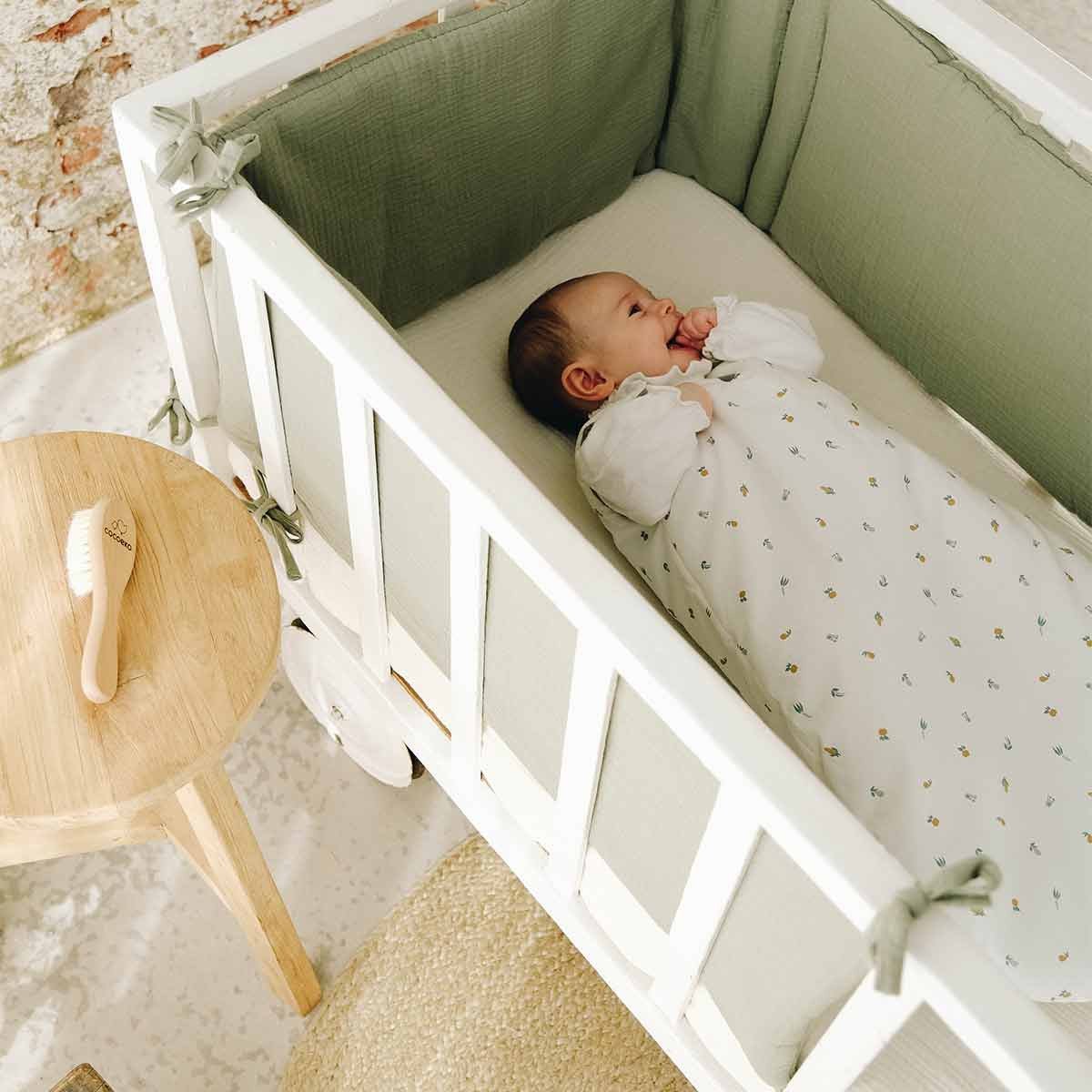 Bed bumper in sage green cotton gauze with a sleeping baby
