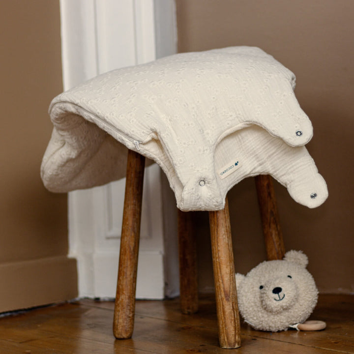 Turbulette tog 2 avec broderies anglaises sur un tabouret avec un doudou dans une chambre de bébé